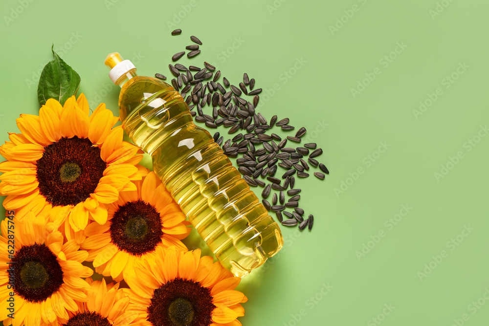 Sunflowers, seeds and bottle of oil on green background