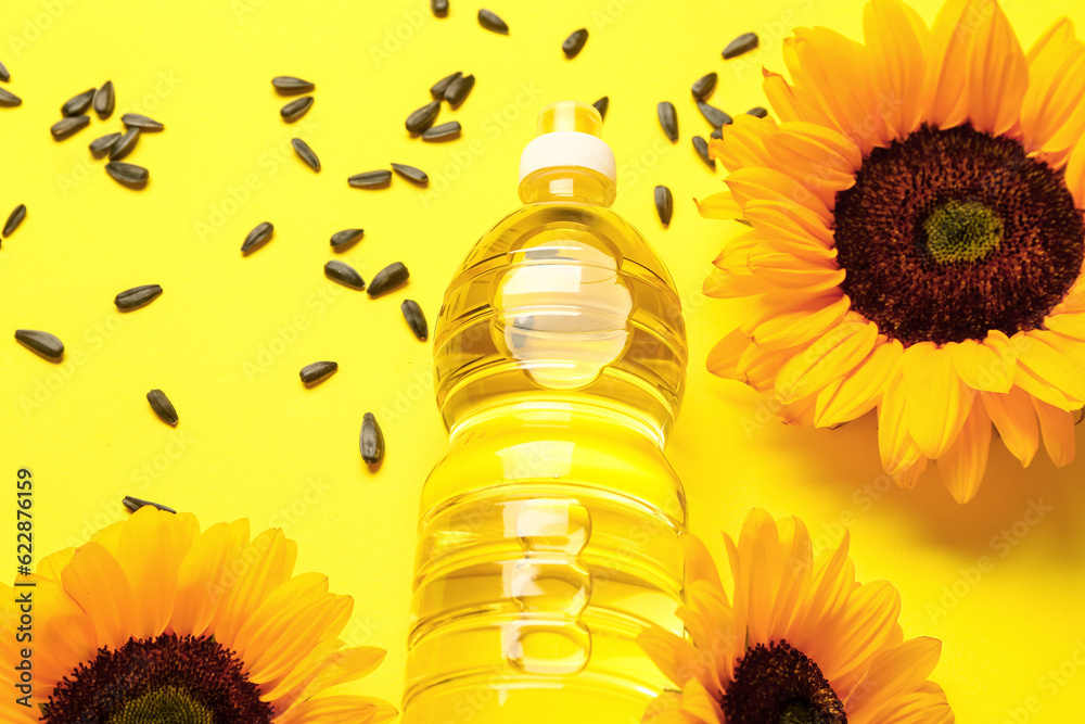 Sunflowers, seeds and bottle of oil on yellow background