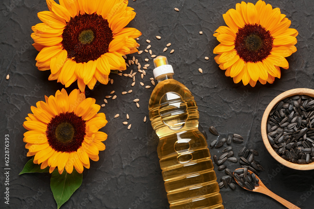 Sunflowers, seeds and bottle of oil on black background