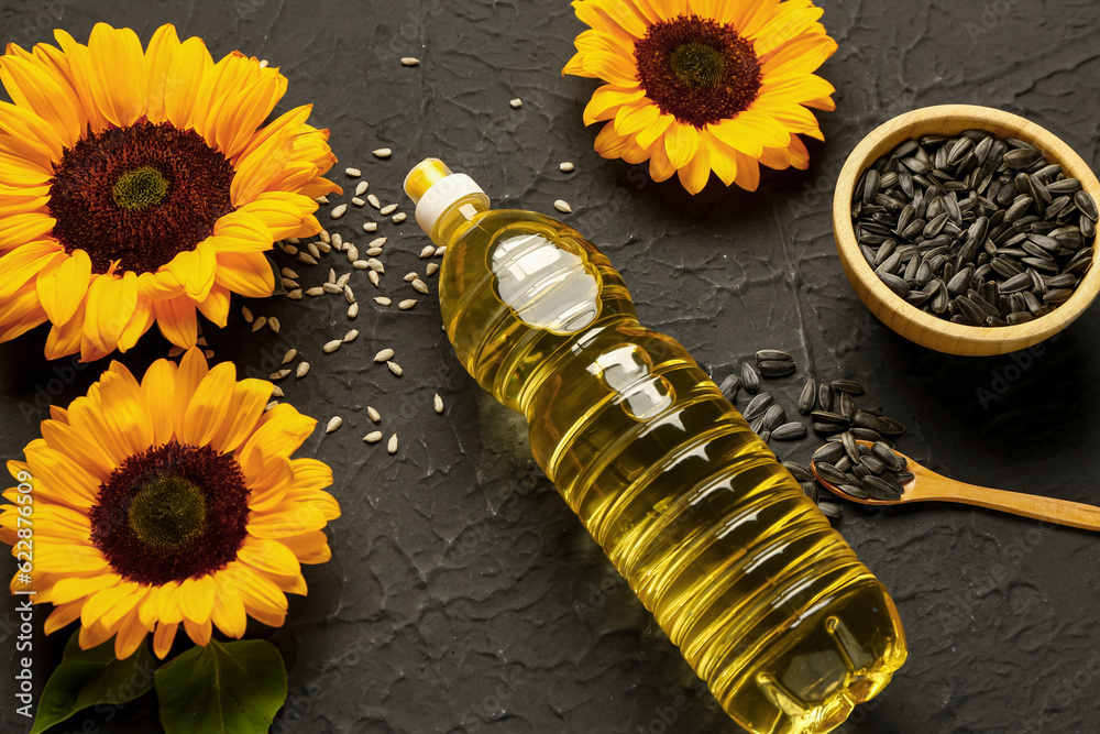 Sunflowers, seeds and bottle of oil on black background