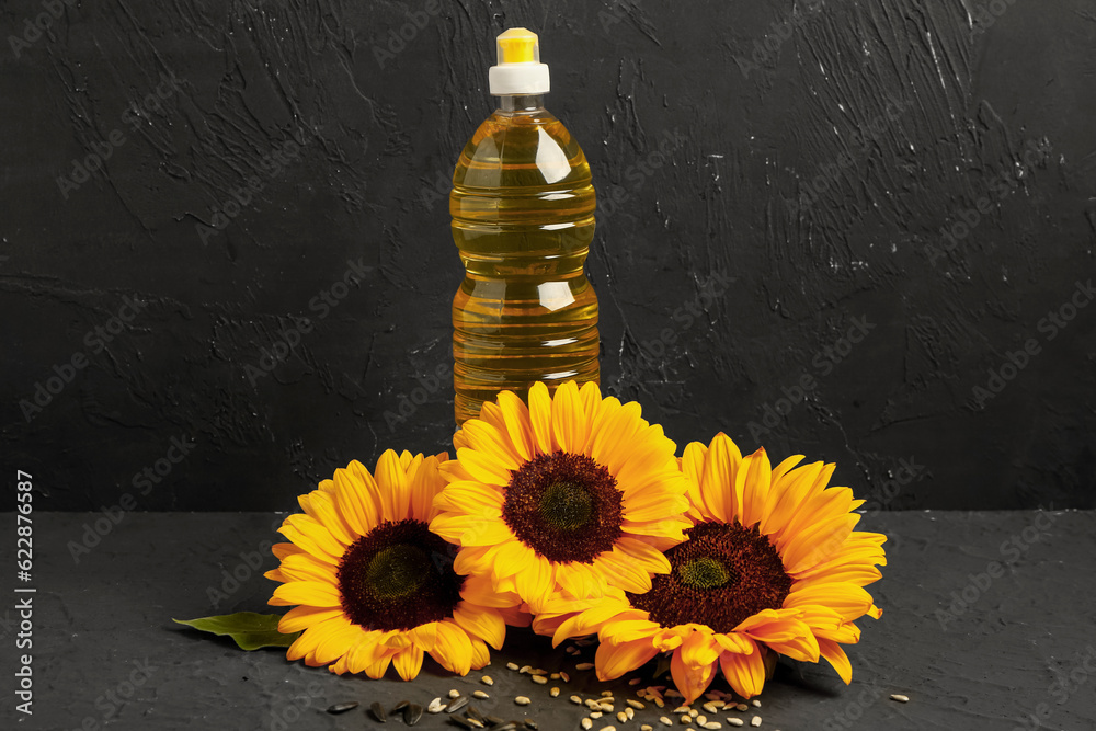 Sunflowers, seeds and bottle of oil on black background