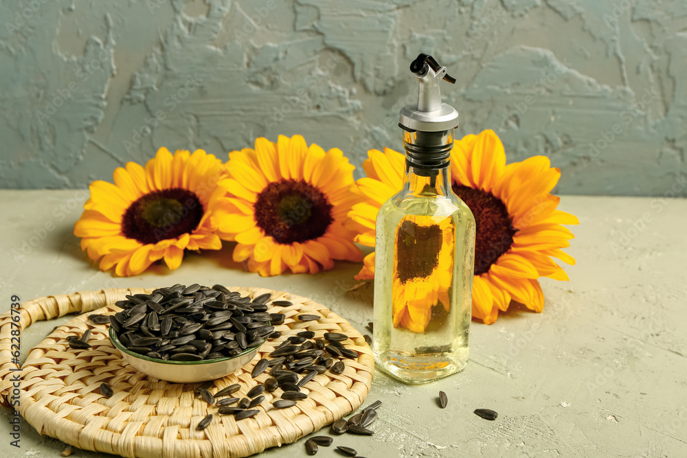 Sunflowers, seeds and bottle of oil on green background