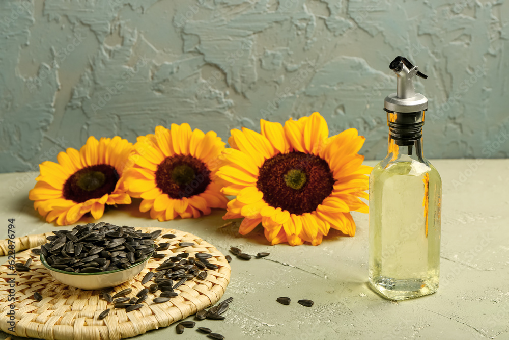 Sunflowers, seeds and bottle of oil on green background