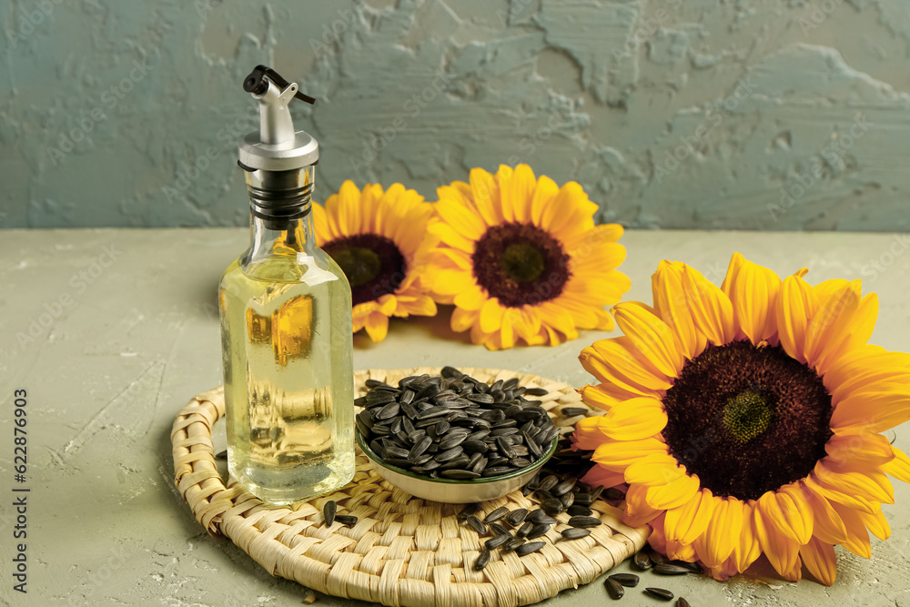 Sunflowers, seeds and bottle of oil on green background