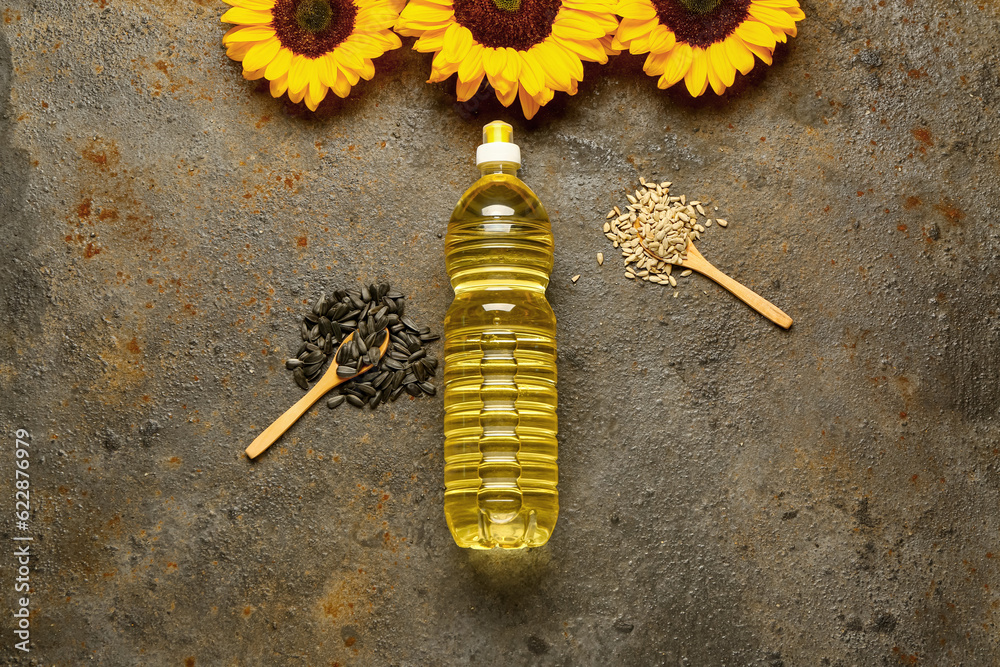 Sunflowers, seeds and bottle of oil on brown background