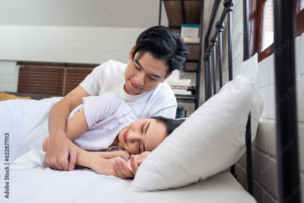 Asian husband kissing his wife while lying down sleep on bed in bedroom. 