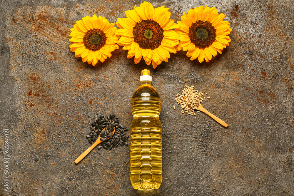 Sunflowers, seeds and bottle of oil on brown background