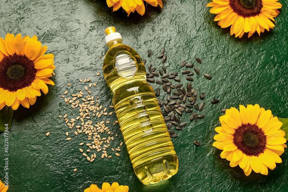 Sunflowers, seeds and bottle of oil on green background