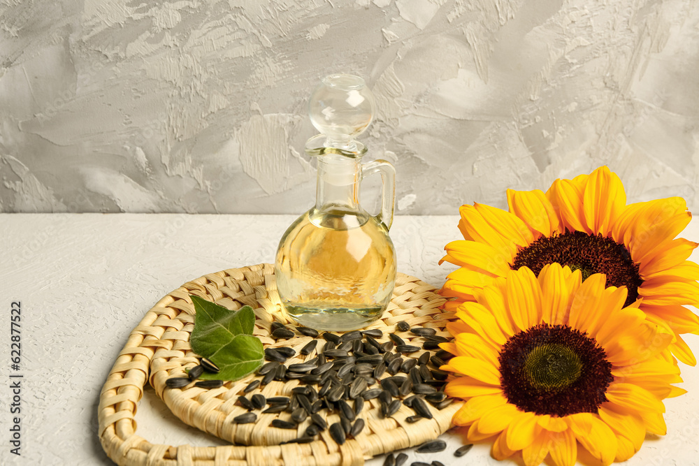 Sunflowers, seeds and decanter of oil on grey background