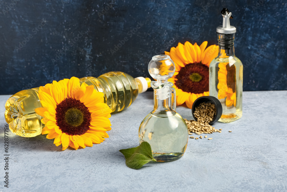 Sunflowers, seeds, bottles and decanter of oil on blue background