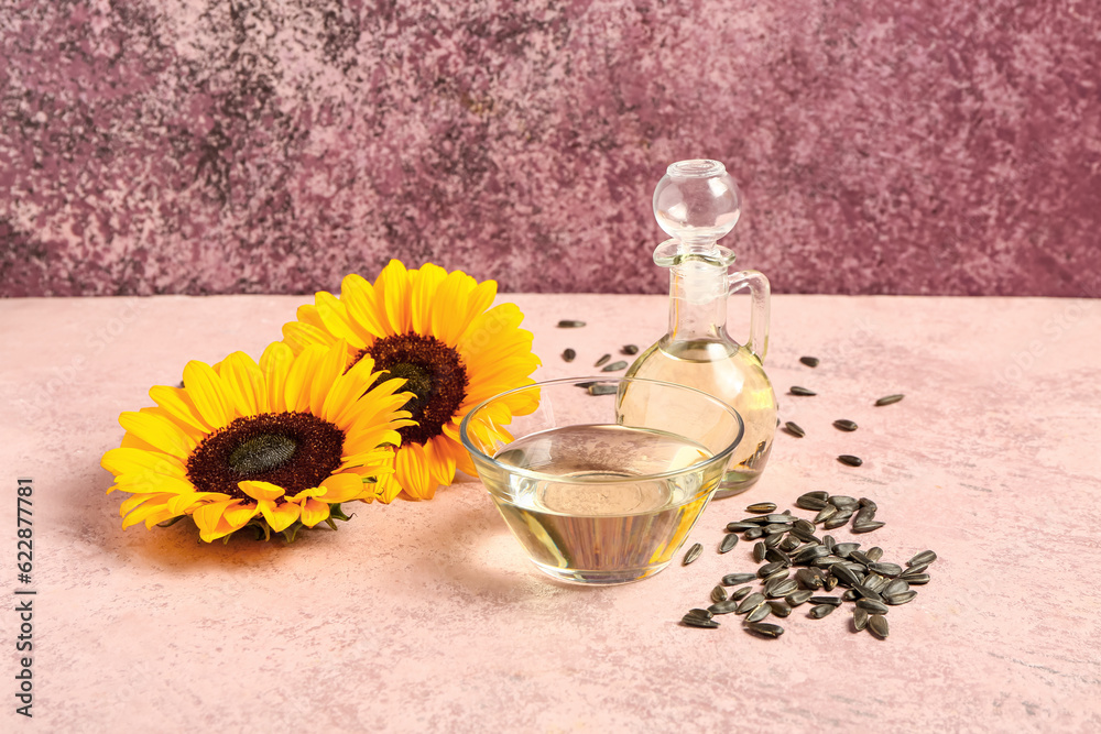 Sunflowers, seeds, bowl and decanter of oil on pink background