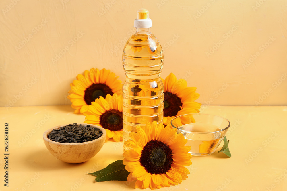 Sunflowers, seeds, bowl and bottle of oil on yellow background