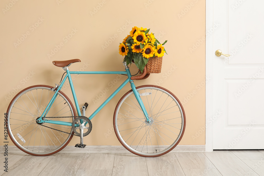 Bicycle with bouquet of beautiful sunflowers in wicker basket near beige wall