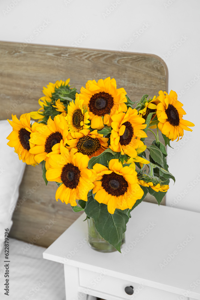 Vase with beautiful sunflowers on bedside table in bedroom