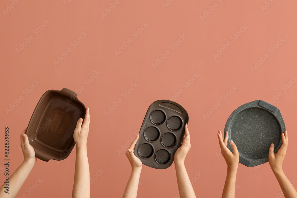 Female hands with different baking forms on pink background