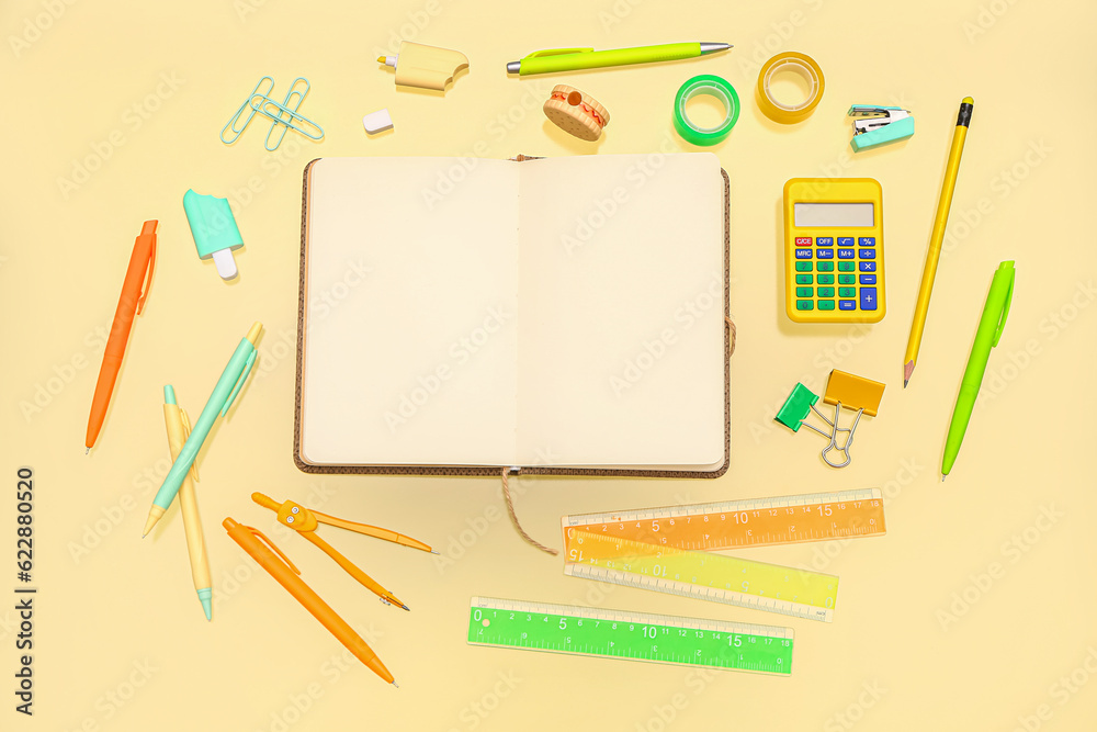 Blank notebook with stationery on pale yellow background