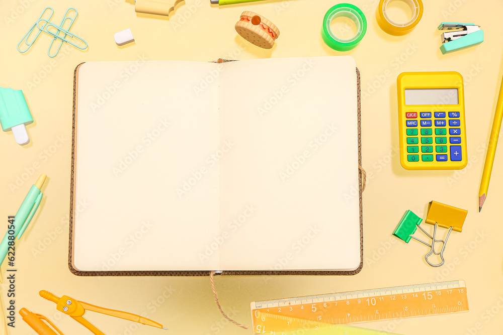 Blank notebook with stationery on pale yellow background