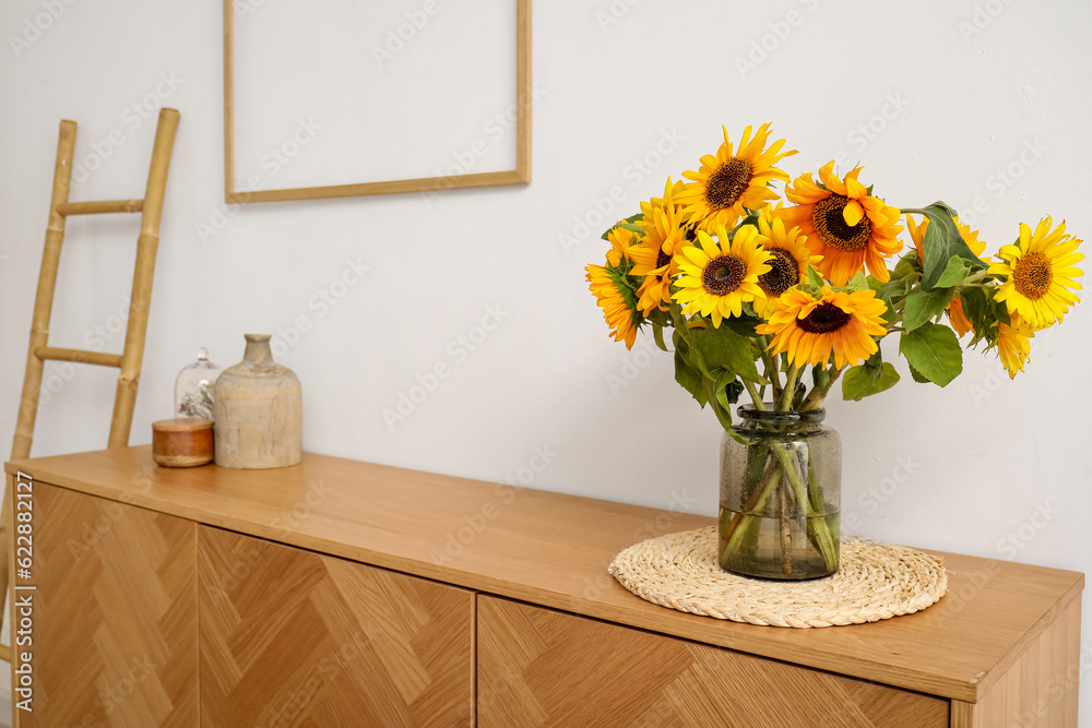 Vase with beautiful sunflowers on wooden cabinet near white wall, closeup