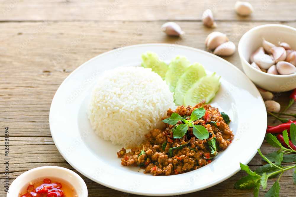 Rice topped with stir-fried pork and basil on wooden table.