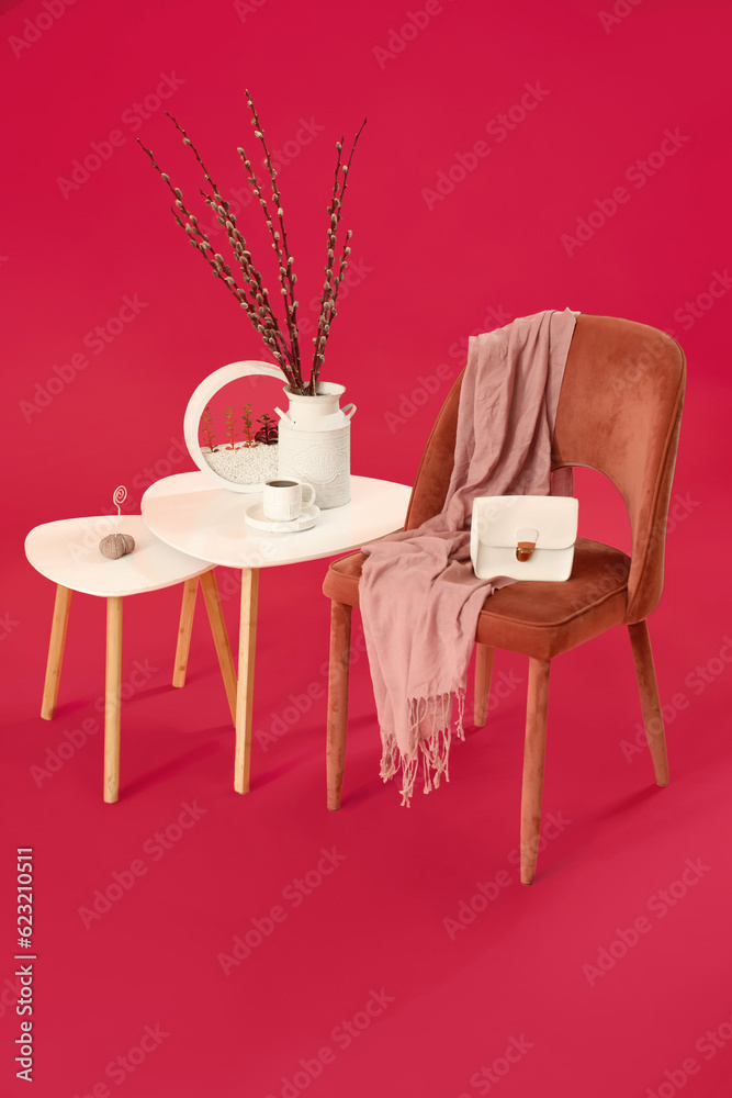 Tables with willow branches, coffee cup, chair and accessories on pink background