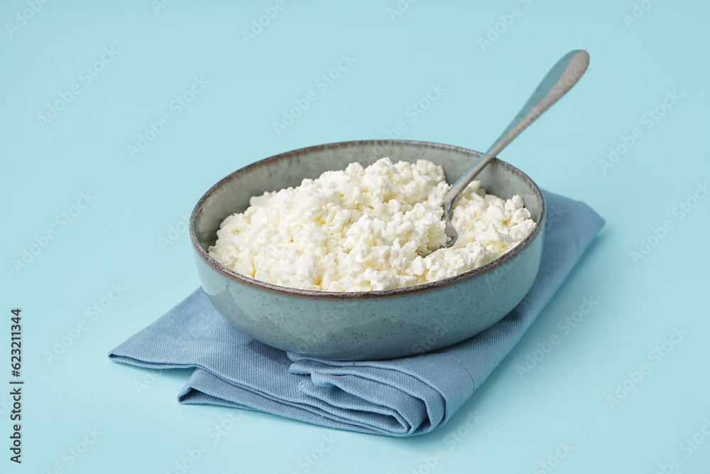 Bowl with tasty cottage cheese on blue background