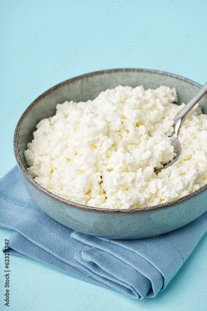 Bowl with tasty cottage cheese on blue background