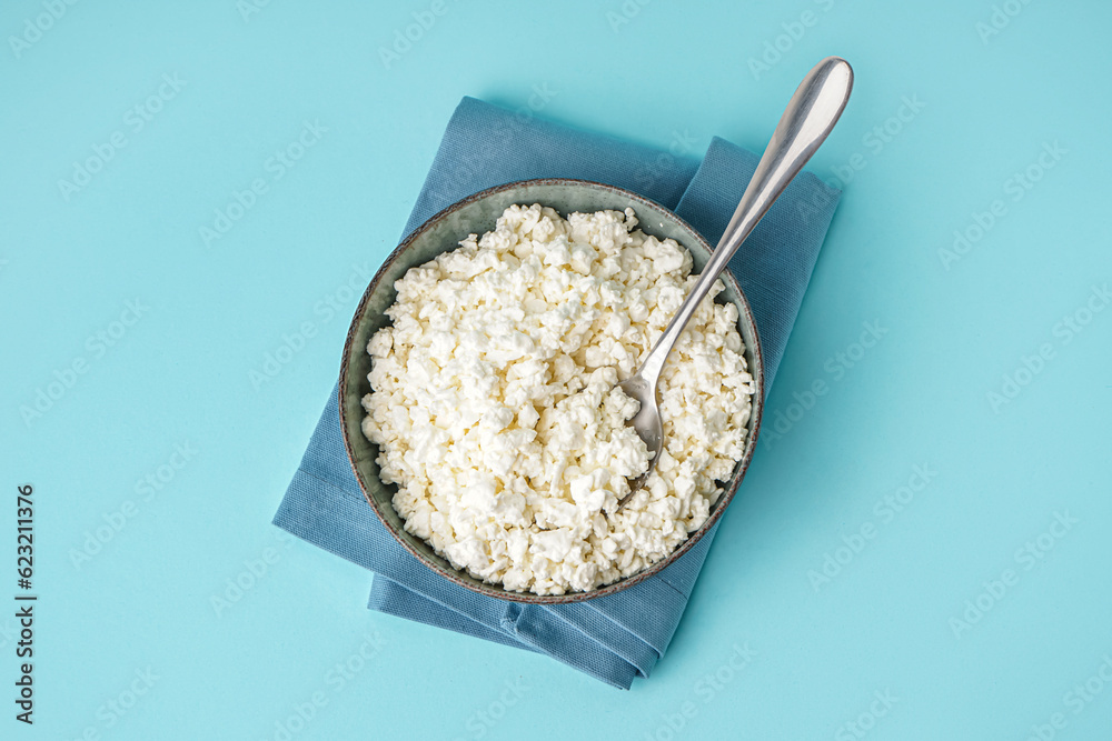 Bowl with tasty cottage cheese on blue background