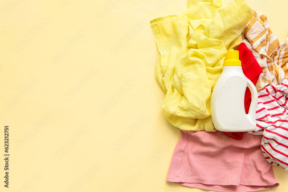 Pile of dirty clothes and bottle of laundry detergent on yellow background