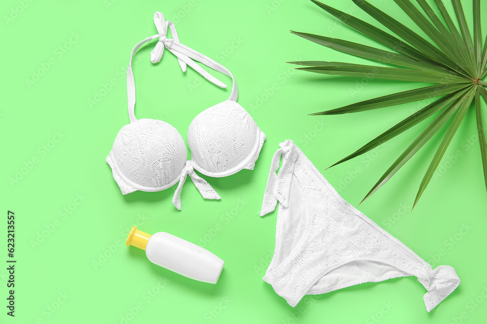 Stylish swimsuit, bottle of sunscreen cream and palm leaf on color background