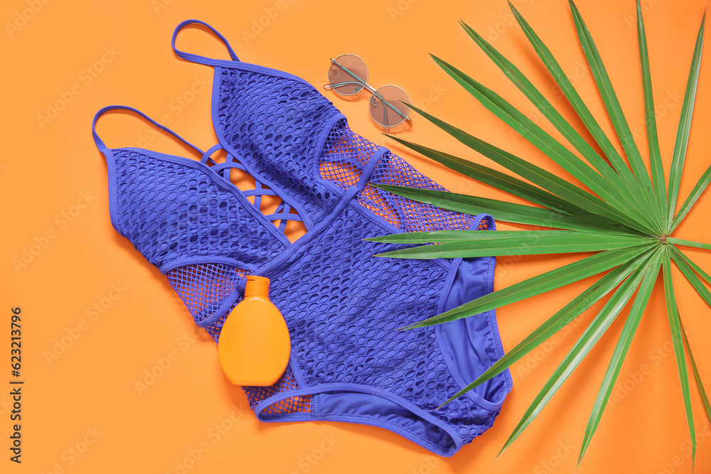 Stylish swimsuit, sunglasses, bottle of sunscreen cream and palm leaf on color background