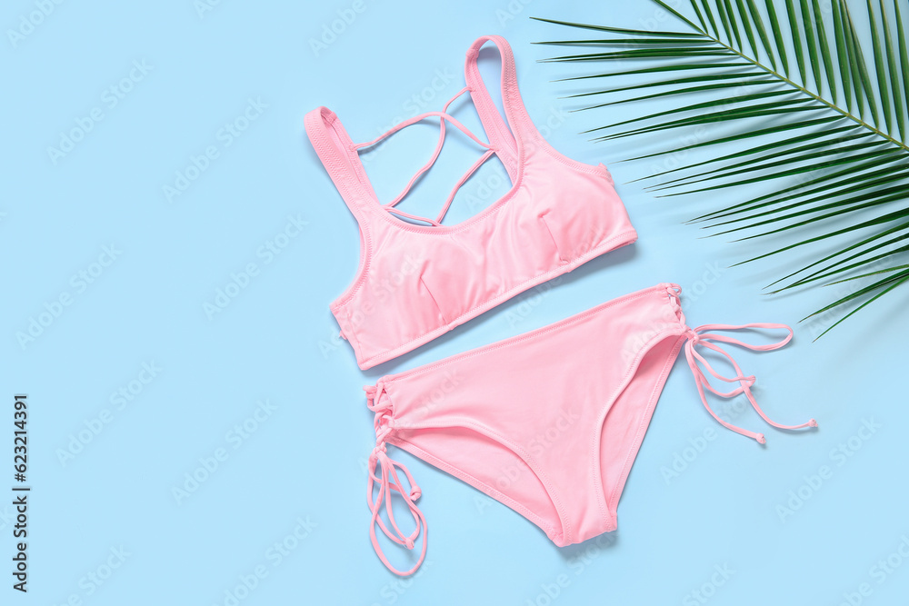 Stylish swimsuit and palm leaf on color background