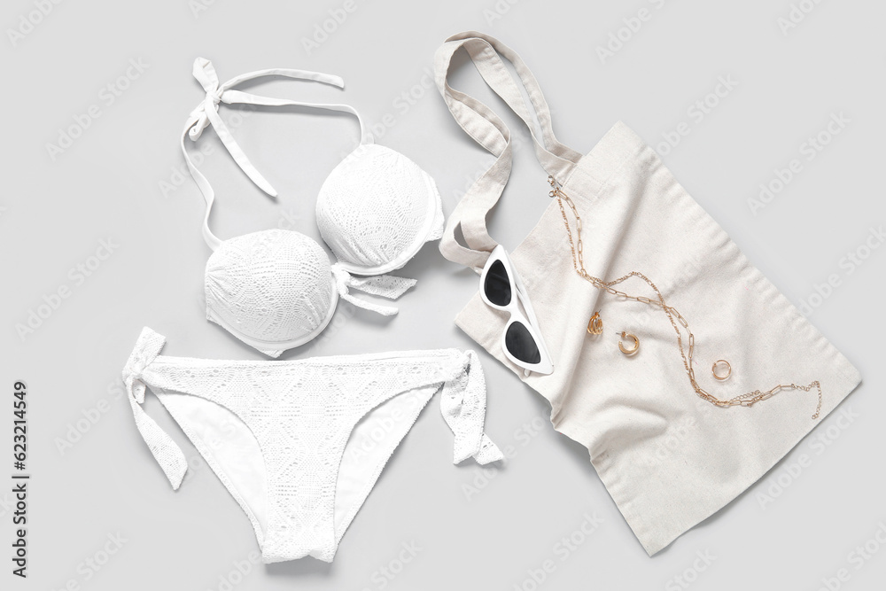 Stylish swimsuit, sunglasses, bag and accessories on light background