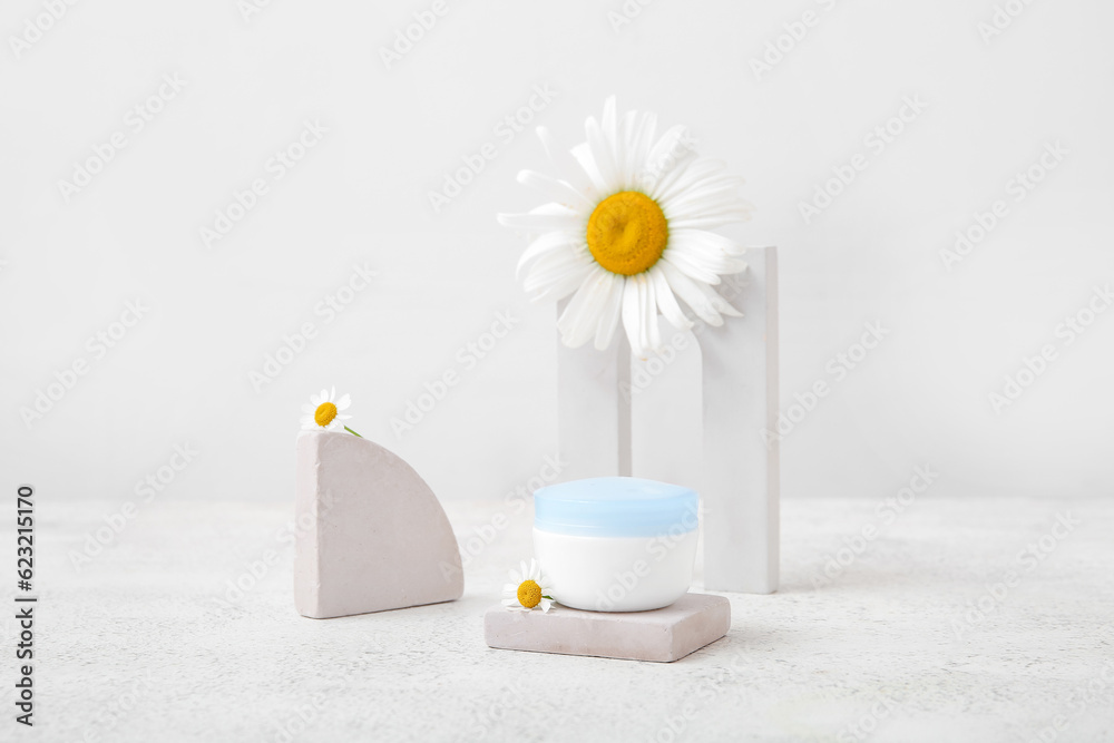 Composition with jar of cosmetic product, plaster podiums and chamomile flowers on light background