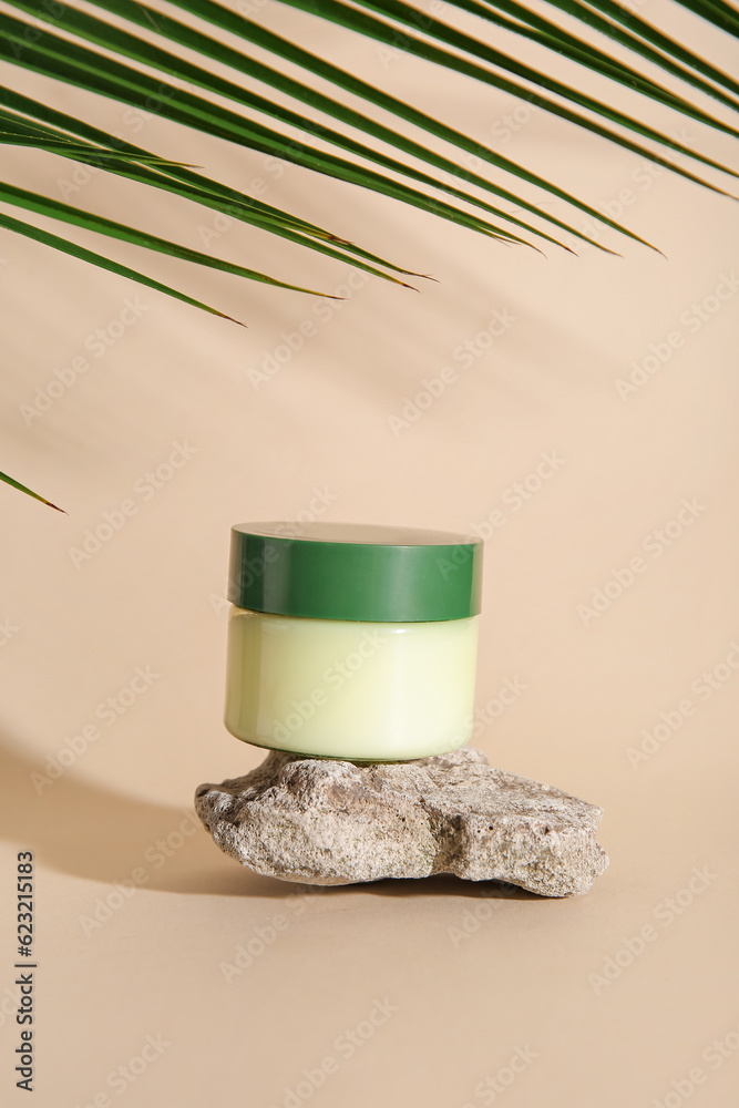 Jar of cosmetic product, stone and palm leaf on color background