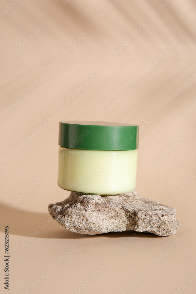 Jar of cosmetic product, stone and palm leaf shadow on color background