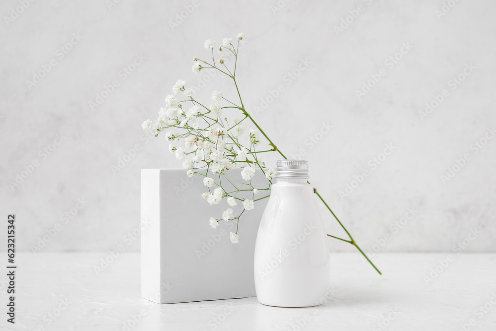 Bottle of cosmetic product, plaster podium and gypsophila flowers on light background