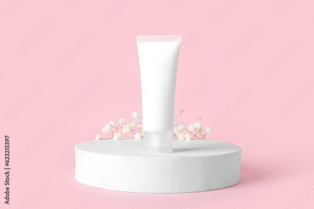 Plaster podium with tube of cosmetic product and gypsophila flowers on pink background