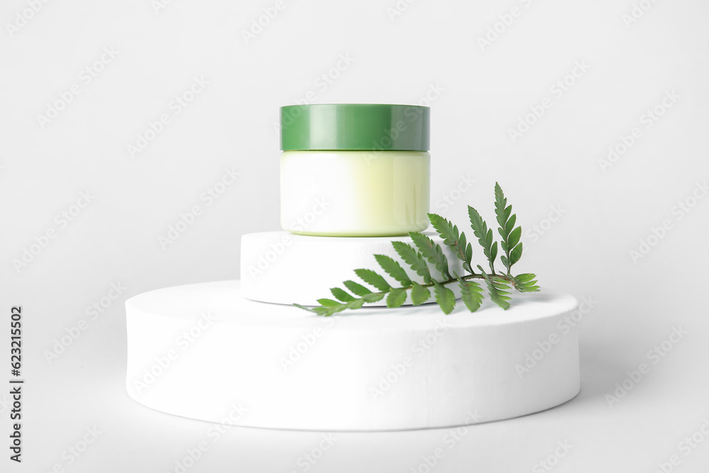 Composition with jar of cosmetic product, plaster podiums and fern leaf on light background