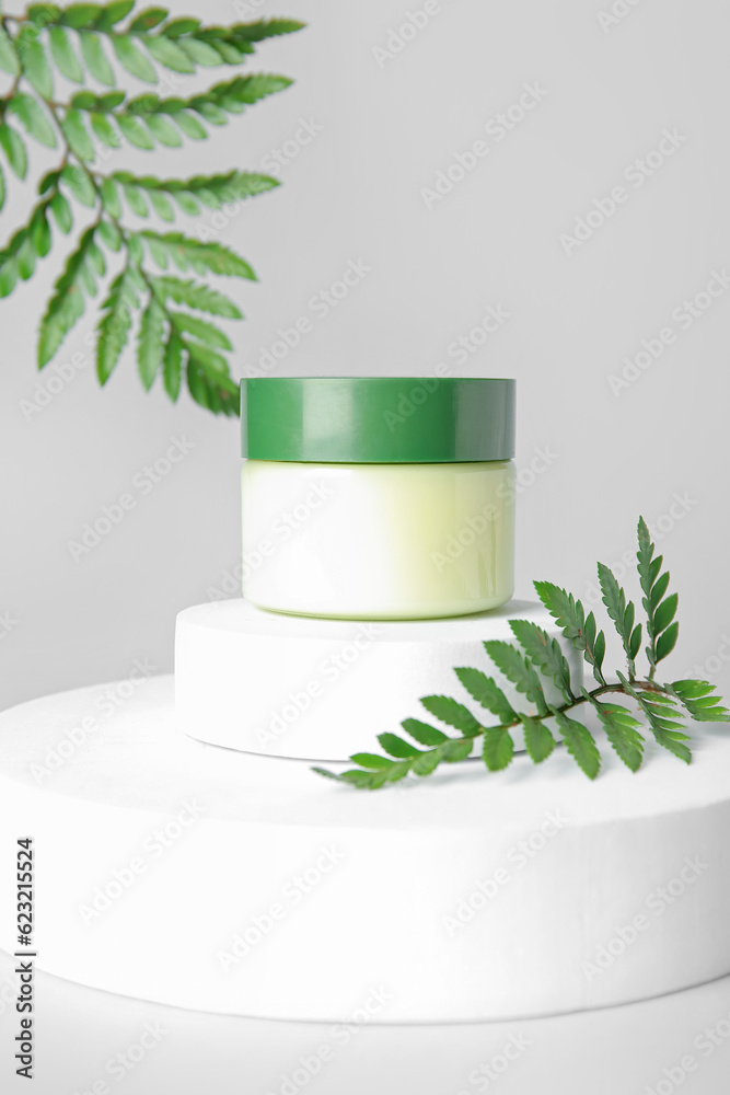 Composition with jar of cosmetic product, plaster podiums and fern leaves on light background