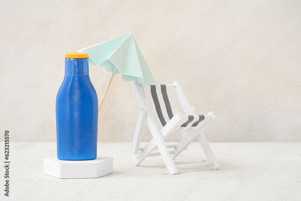 Composition with bottle of sunscreen cream, umbrella and toy deck chair on light background