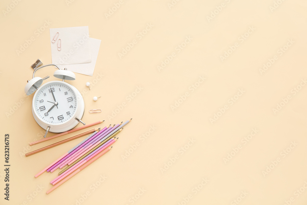 Alarm clock with different stationery on pale orange background