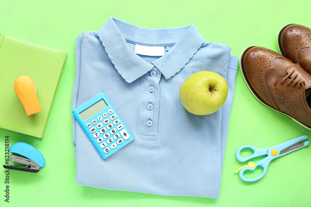 Stylish school uniform with fresh apple and stationery on green background