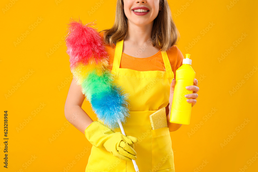 Young woman with bottle of detergent and pp-duster on orange background, closeup