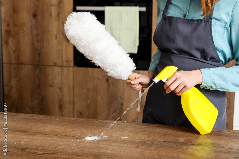 Young woman cleaning table with detergent in kitchen, closeup