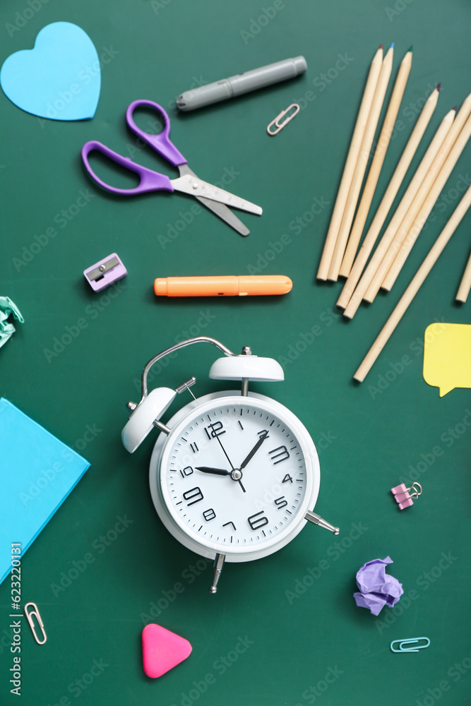 Alarm clock with different stationery on green chalkboard