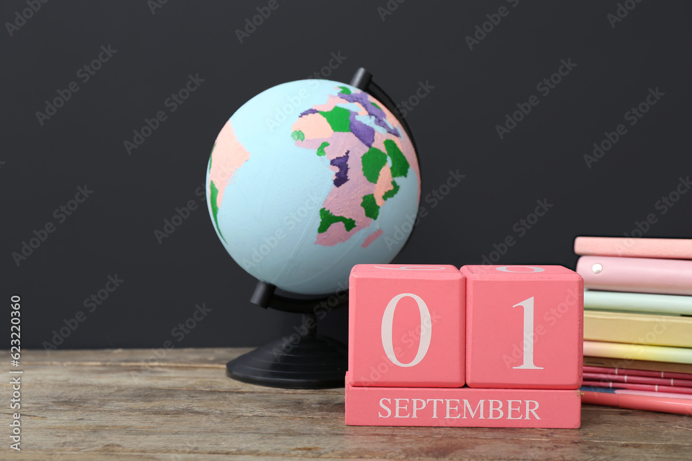 Different stationery, globe and calendar with date SEPTEMBER 1 on wooden table against black chalkbo