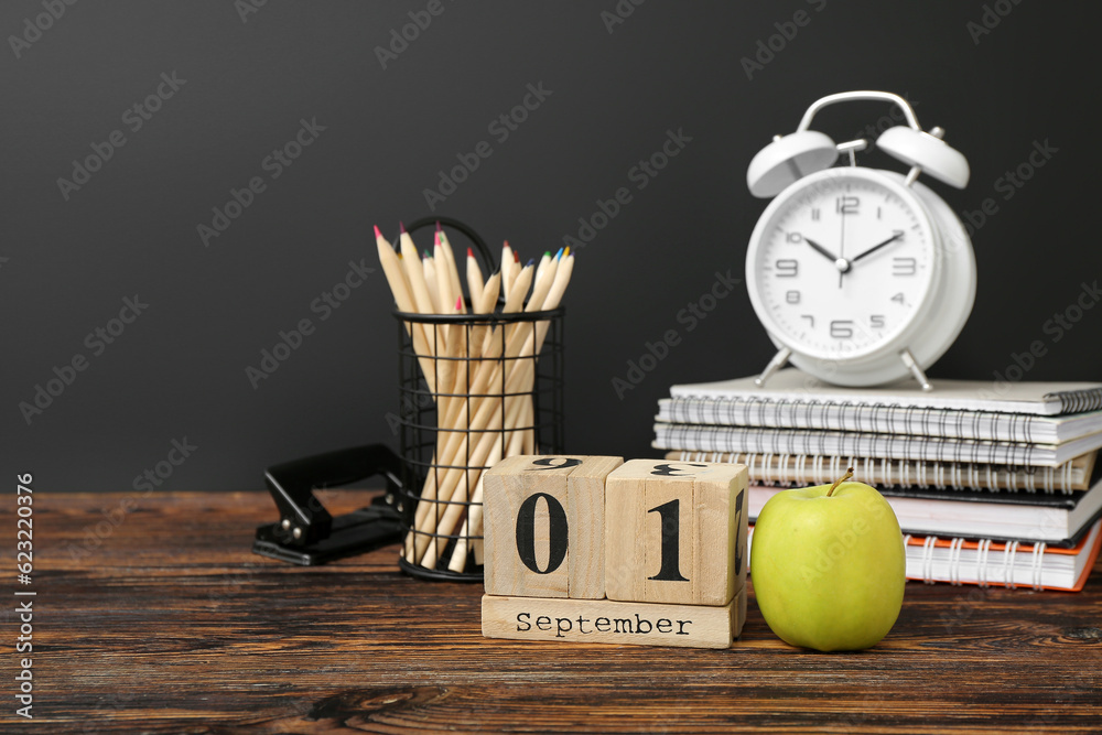 Different stationery, alarm clock and calendar with date SEPTEMBER 1 on wooden table against black c