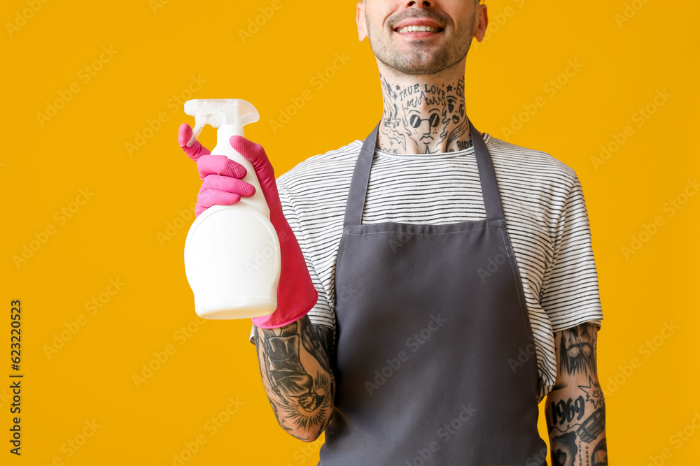 Young tattooed man with bottle of detergent on orange background, closeup