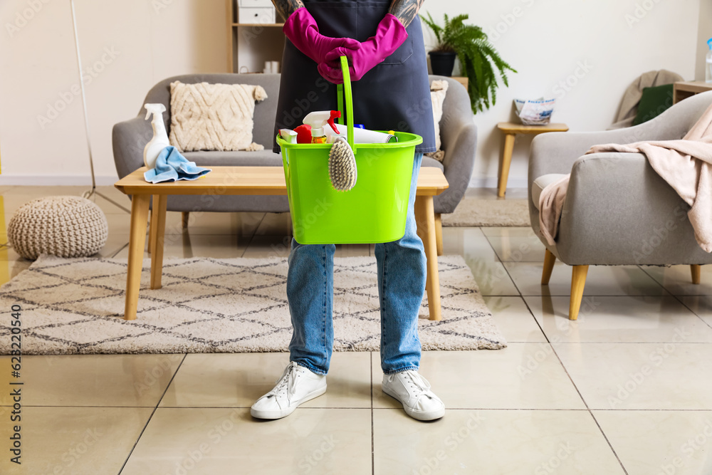 Young tattooed man with bucket of cleaning supplies at home