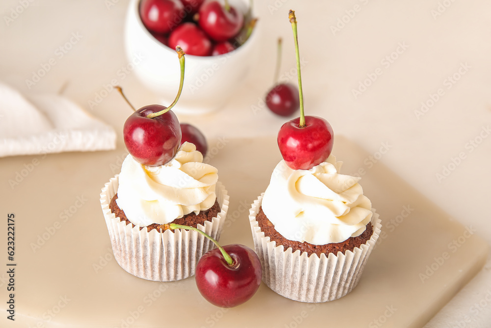 Board with tasty cherry cupcakes on light background